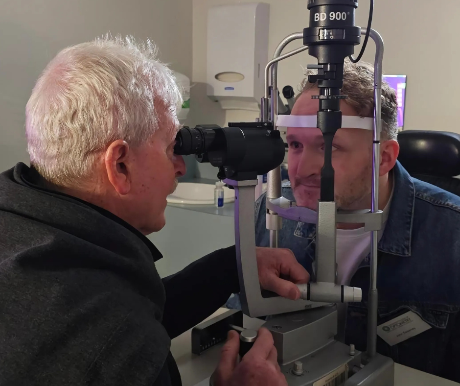 A man looks through the slit lamp eye piece to inspect workshop partner's eye