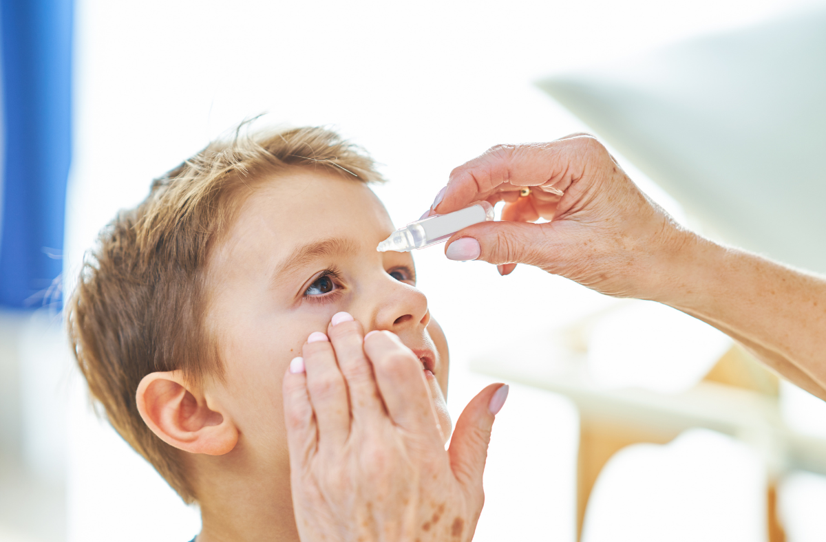 Child has eye drops administered into his eye. 