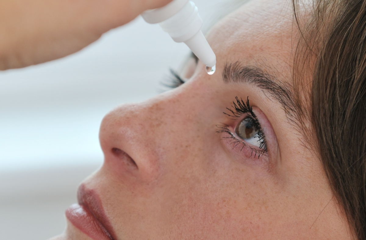 Woman holds a bottle of eye drops above her open eye