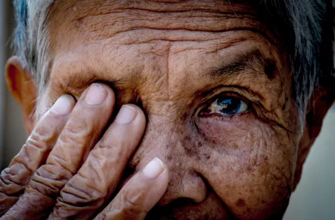 Close-up of an older person’s face with one eye covered by their hand