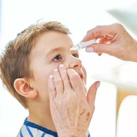 Child has eye drops administered into his eye. 